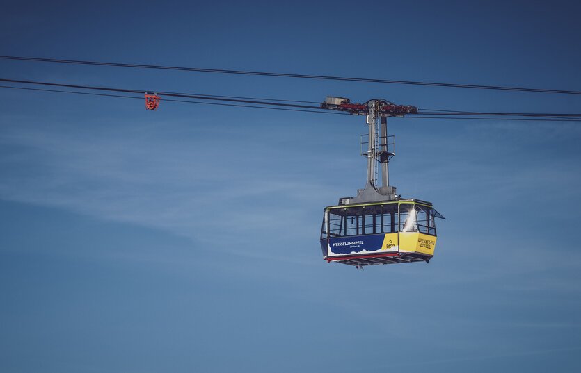 Vor blauem Himmel schwebt die blau/gelbe Gondel der Gipfelbahn zum Weissfluhgipfel auf Parsenn.   | © Davos Klosters Mountains