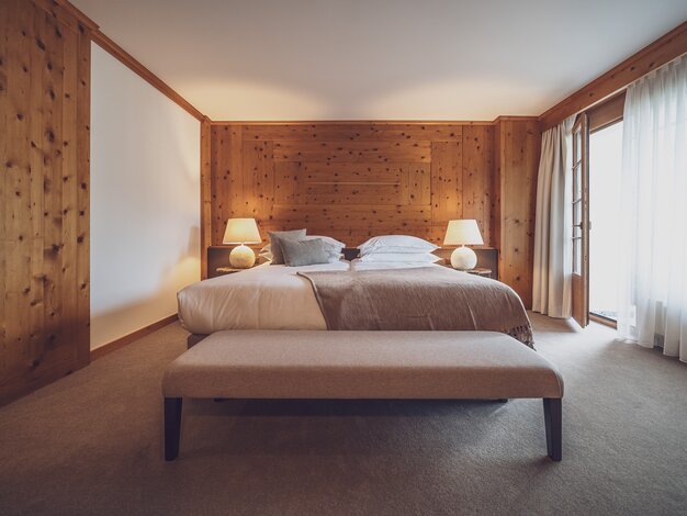 Doppelbettzimmer mit Bettwäsche, Nachttischlämpchen und Kleiderbank  | © Davos Klosters Mountains 